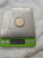 Coin in capsule on digital scale reading 14.10 g