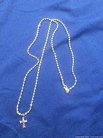 Full view of rope chain necklace with cross pendant laid out on blue fabric