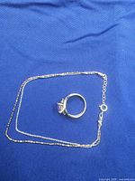 Necklace chain with clasp and ring viewed together on blue fabric