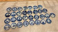 All 32 blue and white Copenhagen Christmas plates laid out in four rows on floor