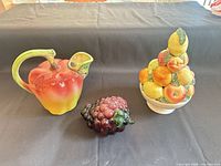 Group shot of ceramic apple pitcher, glass grapes and ceramic fruit basket ornament