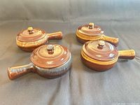 Four ceramic onion soup bowls with lids, brown glaze, one with blue accent