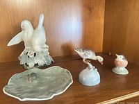 Group of Royal Copenhagen porcelain figurines displayed on shelf: lily pad with frog, small bird, robin, pair of doves