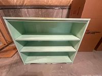 Front view of light green three-shelf wooden bookcase