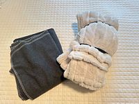 Dark grey fleece throw and rolled beige faux fur throw on quilted surface