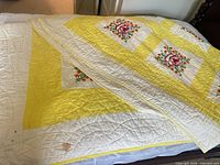 Full view of embroidered quilt folded on bed, partial view of second quilt