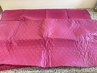 Shows both burgundy quilted table covers laid flat displaying size and pattern