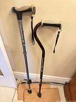 Two Airgo canes standing against wall showing overall form, handles, shafts, straps, and tips