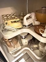 Corner shelf holding spice rack, hand mixers, salad spinner, food processor bases and bowls