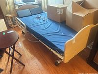 Full view of Joerns bed showing frame, mattress, side rails, headboard, footboard, caster wheels, control pendant and boxes placed on bed
