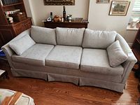 Front view of light grey skirted three-seat sofa with cushions