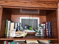 Shelf view showing porcelain jardiniere, parrot figurine on swing, stone bookends and assorted books