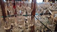 Assorted crystal wine goblets and lowball tumblers on glass shelf
