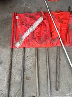 Five rectangular safety flags on wooden handles, red-orange fabric with reflective strip, dirt and wear visible