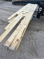 Bundle of pine boards lying on ground, top view shows length and strap