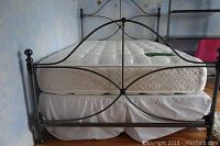 Full view of the bed frame with the mattress on it, showing the design of footboard and side rails with white bed skirt visible.