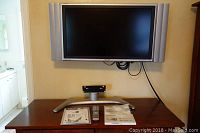 Front view of the Sharp 32 inch TV mounted on the wall above the silver desktop stand with remote control and manual placed on the stand.