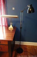 Black floor lamp with adjustable arm and round base standing on wood floor near blue wall