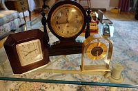 Three vintage clocks on a glass table, including a large Sangamo clock, a Paul Sebastian clock, and a Hampton quartz clock.