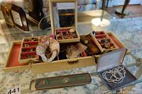 Full view of open folding jewelry case displaying various costume jewelry pieces including earrings, rings, and necklaces, and showing the pearl necklace set on the table next to the case.