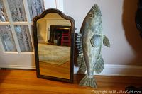Antique wooden framed wall mirror standing on floor next to metal fish wall decor