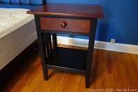 Ethan Allen nightstand positioned next to a bed, showing the full structure including solid cherry wood top and black frame with legs and slatted sides.
