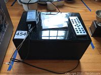 Black rectangular Geneva Sound System Model M unit on wooden floor with power adapter, remote, and manual on top.