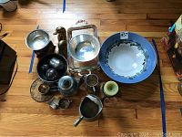 Overview of the lot on wooden floor showing all items including the silver cup, silver plated bowl, bookends, ceramic bowl and coffee pot