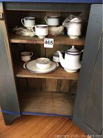 Full view of tea set pieces arranged inside a wooden cabinet, showing teacups, saucers, plates, teapot, sugar bowl, creamer, and charger.