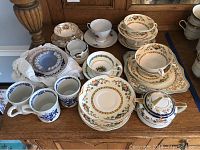 Overview showing multiple cups, saucers, plates arranged on a wooden surface, including Johnson Brothers Pareek pattern pieces and assorted other china items.