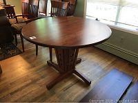 Round cherry dining table with smooth finish on top and four chairs partially visible.