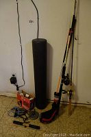 Photo shows three golf clubs, two fishing poles, a black foam roller, and a box with vintage Princess Smart Belles weight set along with other exercise accessories on the floor next to a white wall.