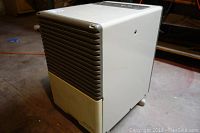 Side angle view showing front grey vent slats and white body with wear marks, on concrete floor.