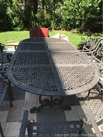 Full-top view of rectangular lattice-patterned table on patio with surrounding chairs and garden background