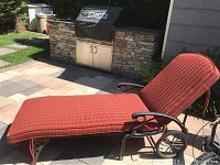 Front and side view of the metal patio lounge chair with red upholstered cushion and visible wheels on a stone tile patio.