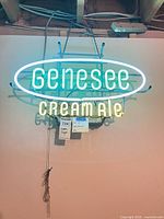 Front view of illuminated Genesee Cream Ale neon sign hanging from ceiling joist