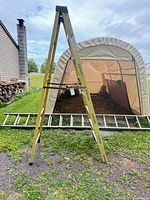 Overall view of yellow fiberglass A-frame ladder standing, aluminum extension ladder lying on ground