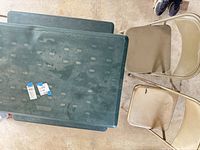 Top view of green folding picnic table, visible stain patterns, two beige folding metal chairs