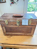Front view of closed oak tool chest showing brass hardware, leather handle, dimension note