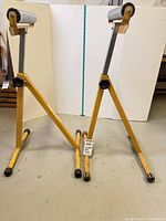 Pair of yellow steel telescoping roller stands folded open showing rollers, legs, knobs and wear