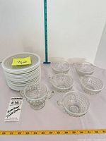 Stack of white plates beside clear hobnail glass bowls and footed piece