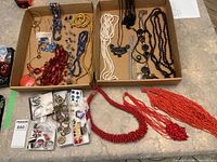 Overview of two trays with assorted necklaces, earrings, rings and red seed bead necklace on counter