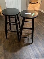 Two black wooden bar stools on dark floor