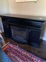 Full view of black wooden electric fireplace console showing side cabinets, open shelf, insert