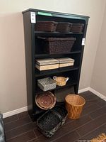 Front view of black wooden shelf unit with baskets and boxes displayed on shelves and floor