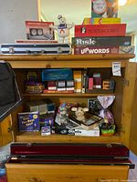 Full cabinet view showing board games, figurines, chess clock, playing cards, aluminum case, banner partly visible