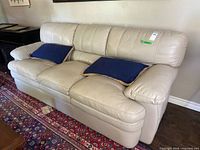 Front view of cream leather three-seat sofa with two navy blue pillows