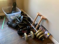 Overall view of lot showing dumbbells, barbell, parallettes, resistance bands, foam roller, ab roller, belt, DVDs and storage bin with plates