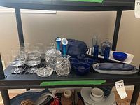 Shelf with clear glasses, crystal dishes, blue ceramic casserole, rooster divided dish, blue vases, bottles, candlesticks