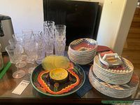 Full lot view showing dinnerware stacks, stemware, tumblers, platter, bowl, green plates, placemats and hamburger press